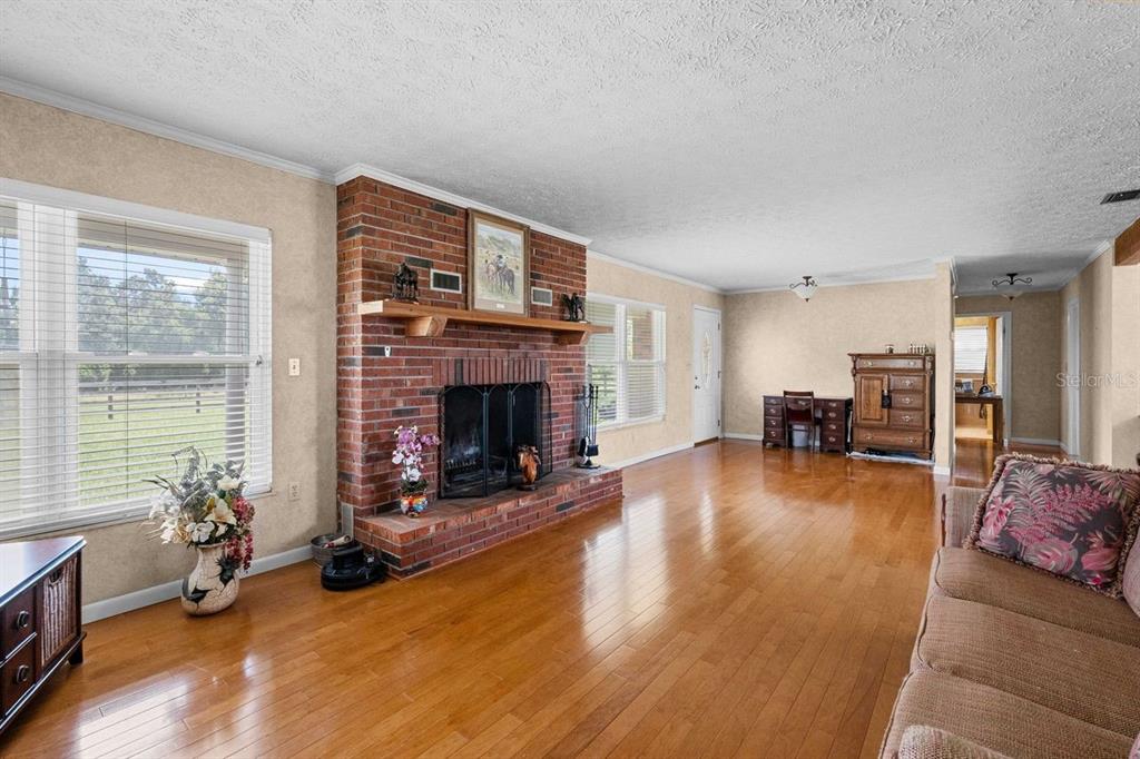 A living room with hardwood floors, a brick fireplace, and a large window — 38730 MICKLER ROAD, DADE CITY, FL