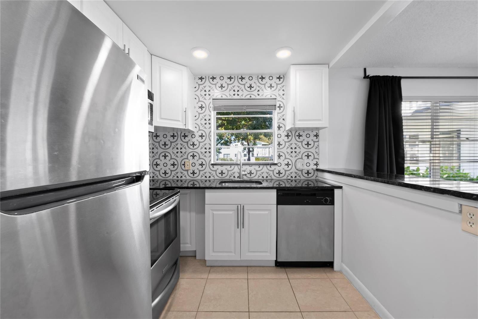 A kitchen features white cabinets, patterned tile backsplash, stainless steel appliances, and black countertops — 28 Prescott B # 28, Deerfield Beach FL 33442, DEERFIELD BEACH, FL