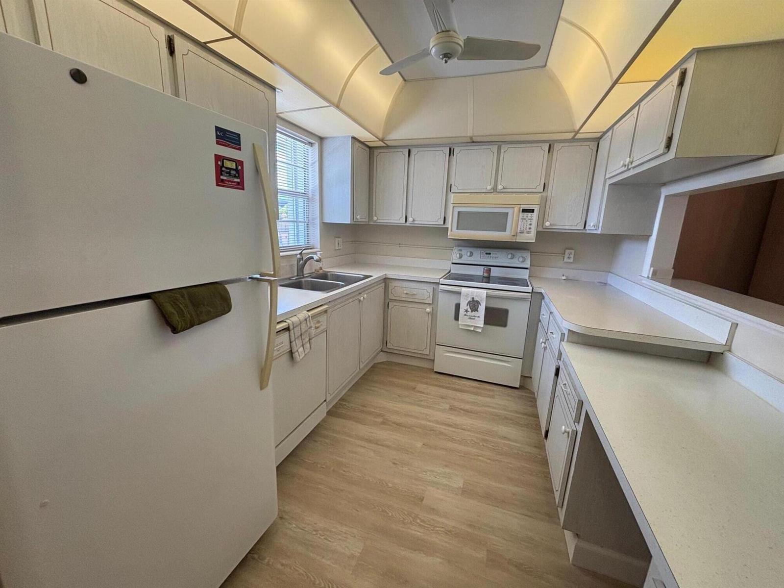 A kitchen features white cabinets, white appliances, light countertops, and light wood-look flooring — 2950 SE Ocean Boulevard # 5, Stuart FL 34996, STUART, FL