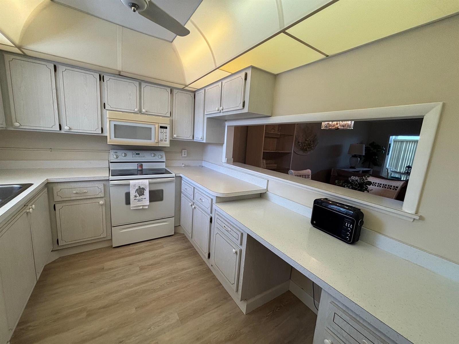 A kitchen with white cabinets, light countertops, a pass-through window, and light wood-look flooring — 2950 SE Ocean Boulevard # 5, Stuart FL 34996, STUART, FL