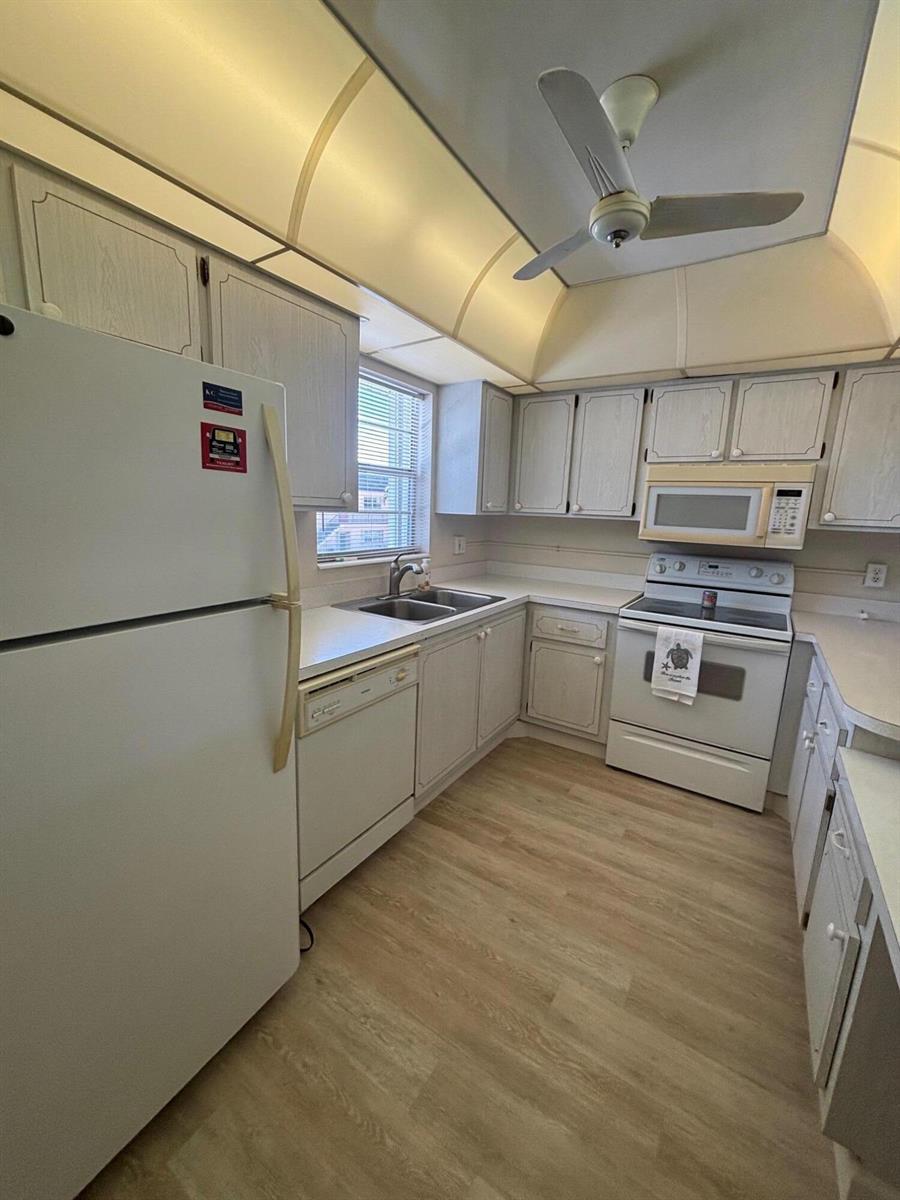 A kitchen features white cabinets, light-colored wood-look flooring, and white appliances under a vaulted ceiling — 2950 SE Ocean Boulevard # 5, Stuart FL 34996, STUART, FL