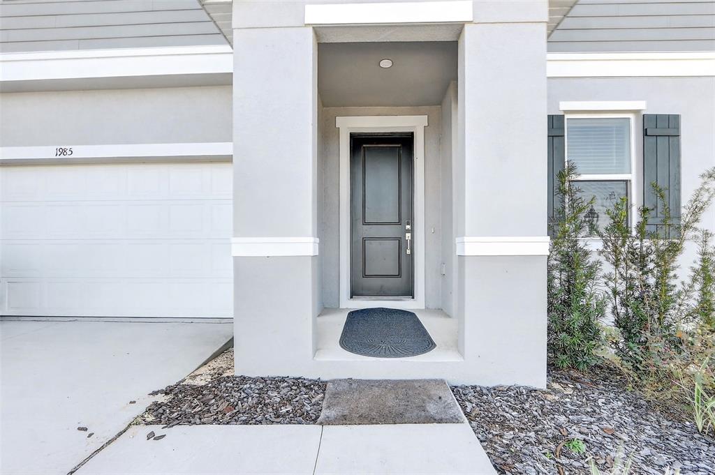 The exterior of a house features a gray front door, a garage, and landscaping — 1985 BURGUNDY DRIVE, MINNEOLA, FL
