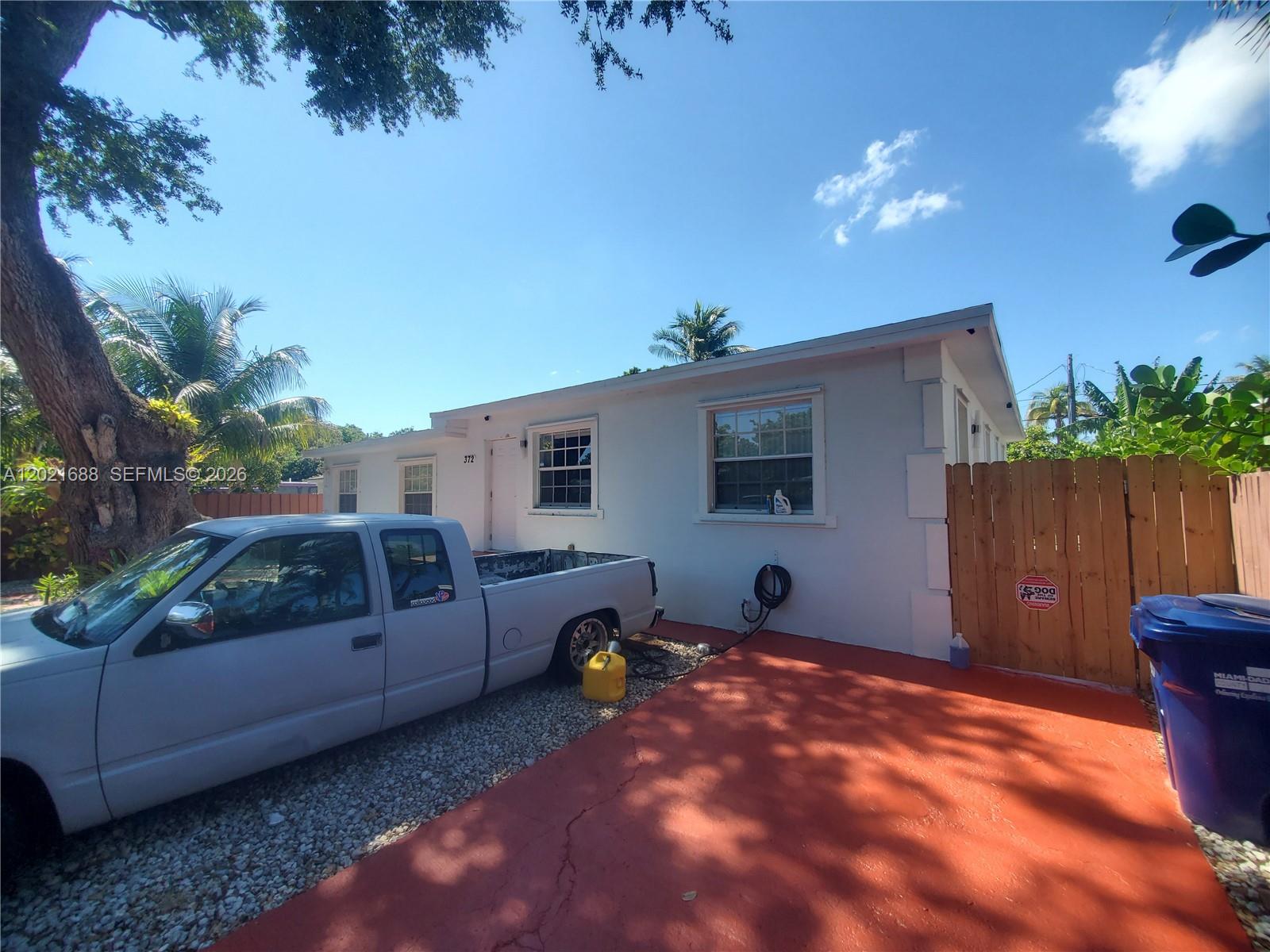 A white single-story house with a gravel driveway, a red concrete pad, and a wooden fence — 372 NE 162nd St, Miami FL 33162, MIAMI, FL