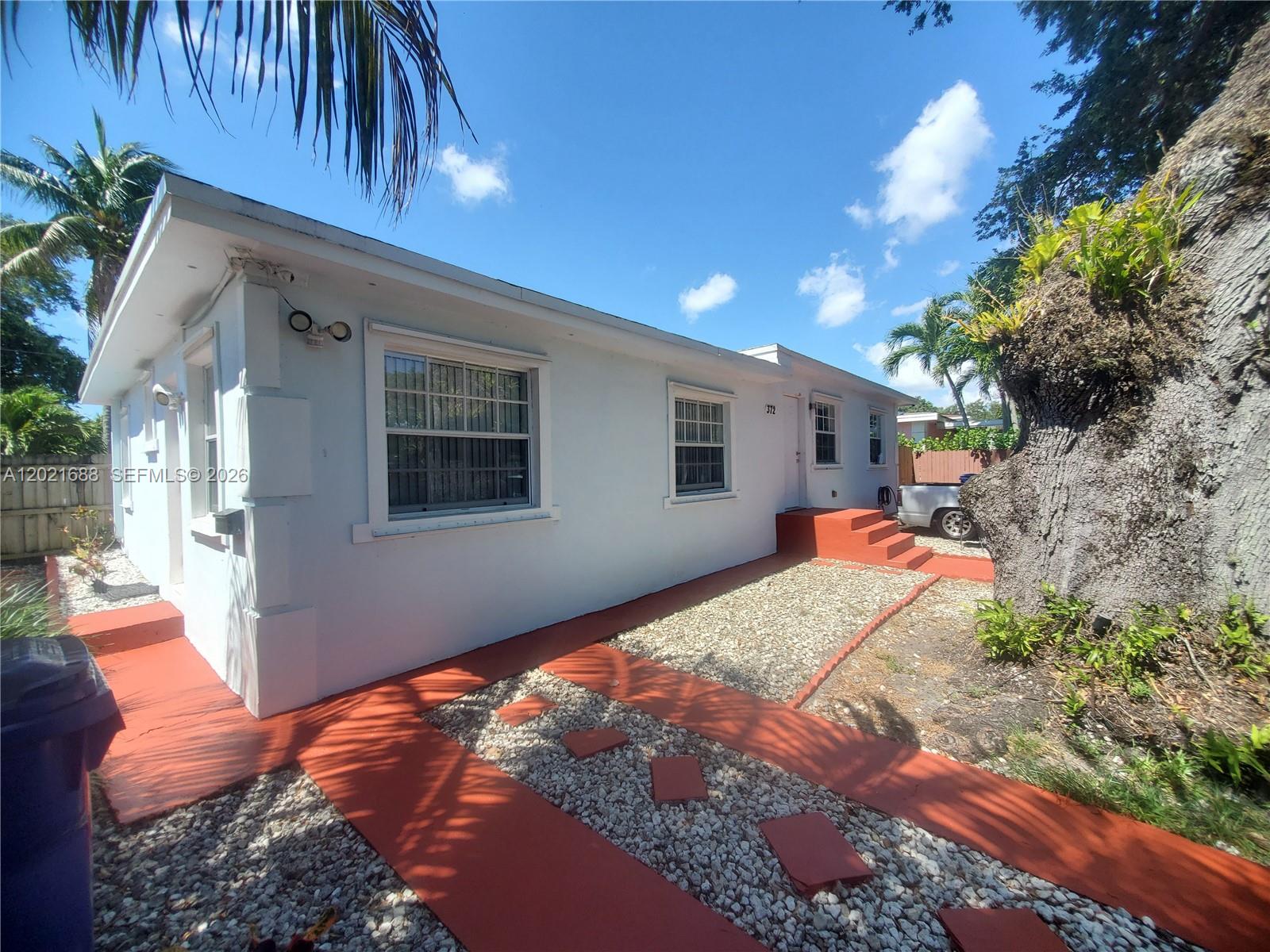 A white single-story house features a red-painted walkway and steps with gravel landscaping — 372 NE 162nd St, Miami FL 33162, MIAMI, FL