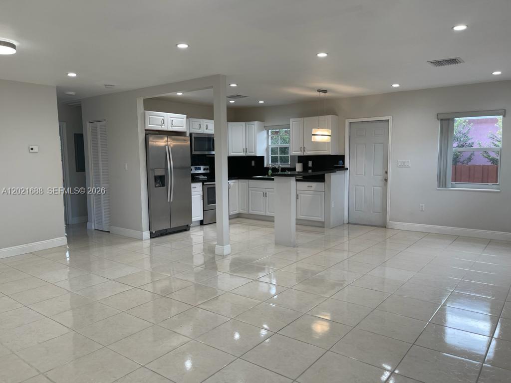 A kitchen with white cabinets, stainless steel appliances, and tile flooring opens to a living area — 372 NE 162nd St, Miami FL 33162, MIAMI, FL
