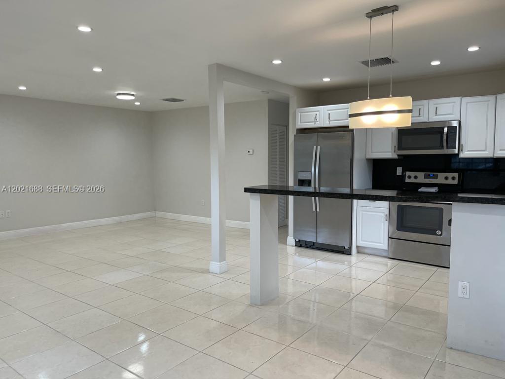 A kitchen with stainless steel appliances and white cabinets overlooks an open-concept tiled living area — 372 NE 162nd St, Miami FL 33162, MIAMI, FL