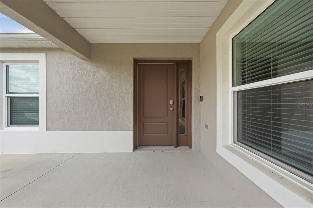 A covered concrete entryway features a brown front door with a side window — 6094 RODRIGUEZ LANE, THE VILLAGES, FL