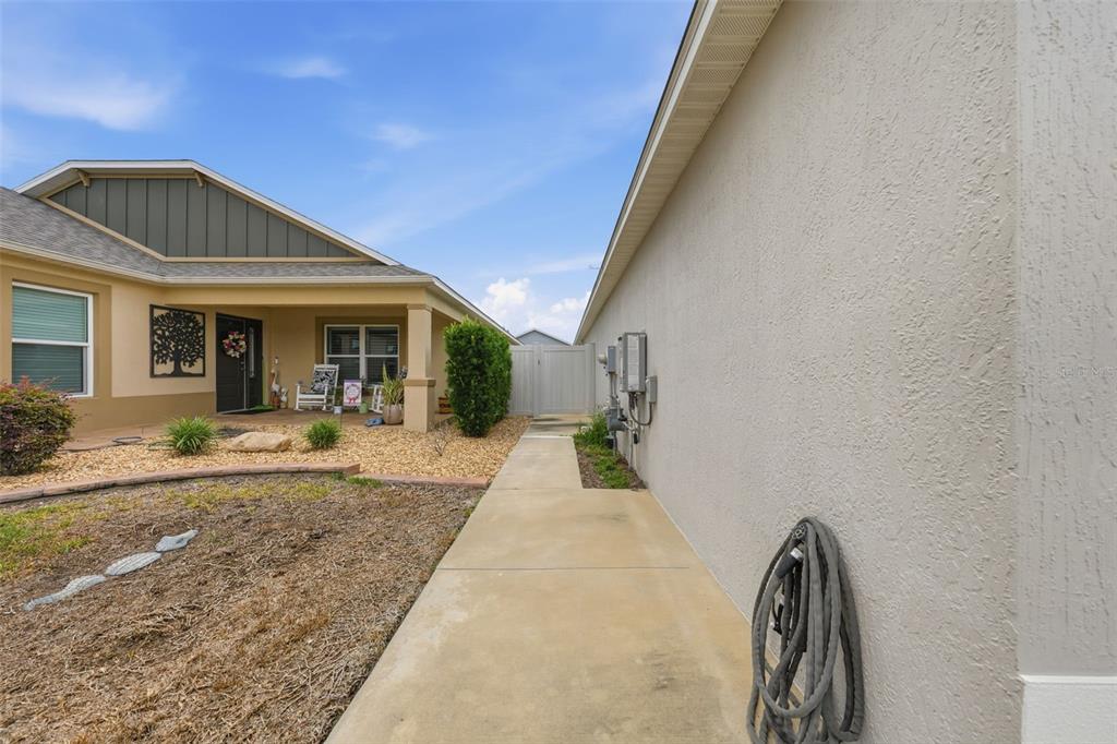 A concrete walkway leads between a house exterior and a side yard toward a gate — 6094 RODRIGUEZ LANE, THE VILLAGES, FL