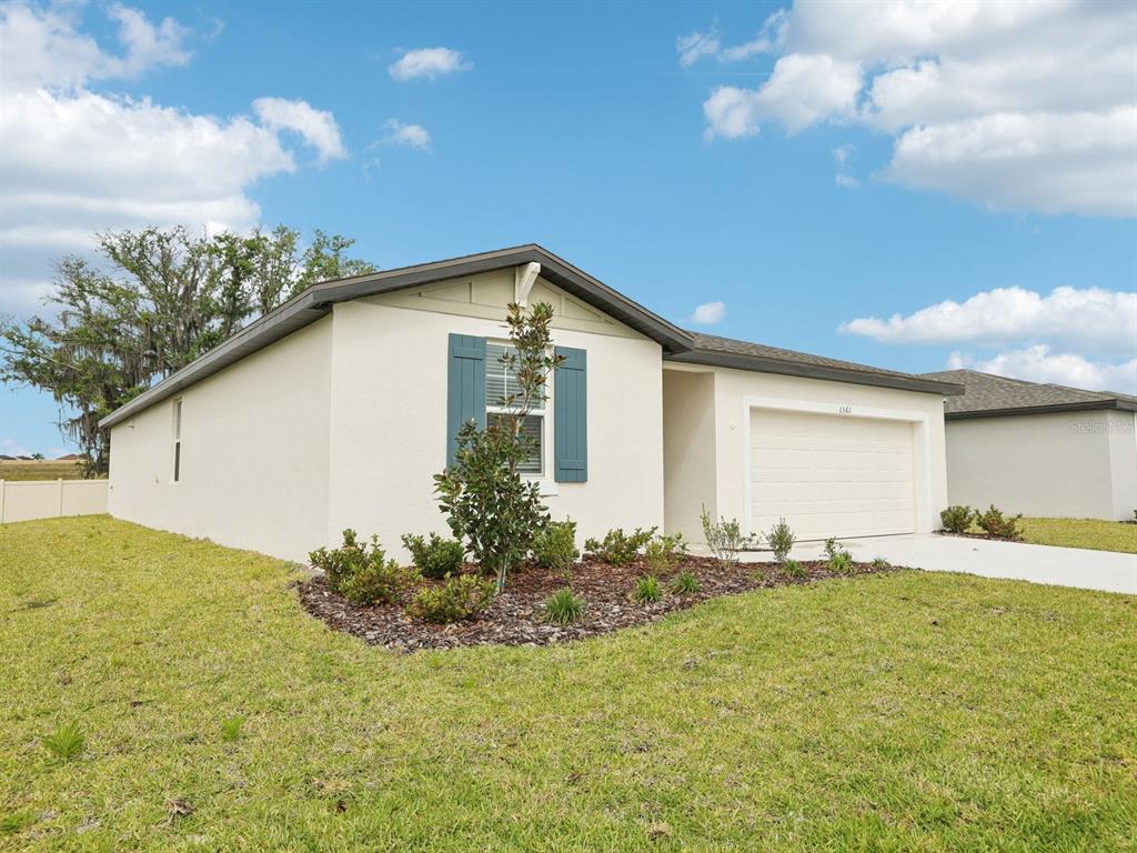 A single-story house with a white stucco exterior, blue shutters, and an attached garage — 1361 OAK VALLEY DRIVE, AUBURNDALE, FL