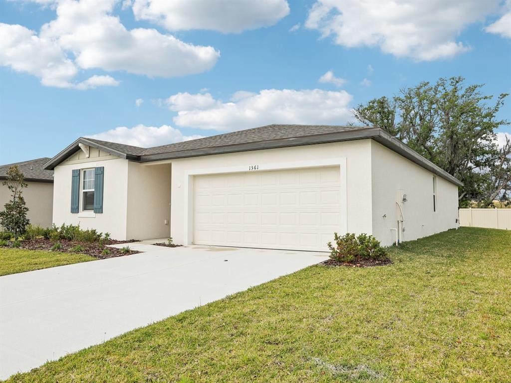 A single-story house with a white stucco exterior, a two-car garage, and blue shutters — 1361 OAK VALLEY DRIVE, AUBURNDALE, FL