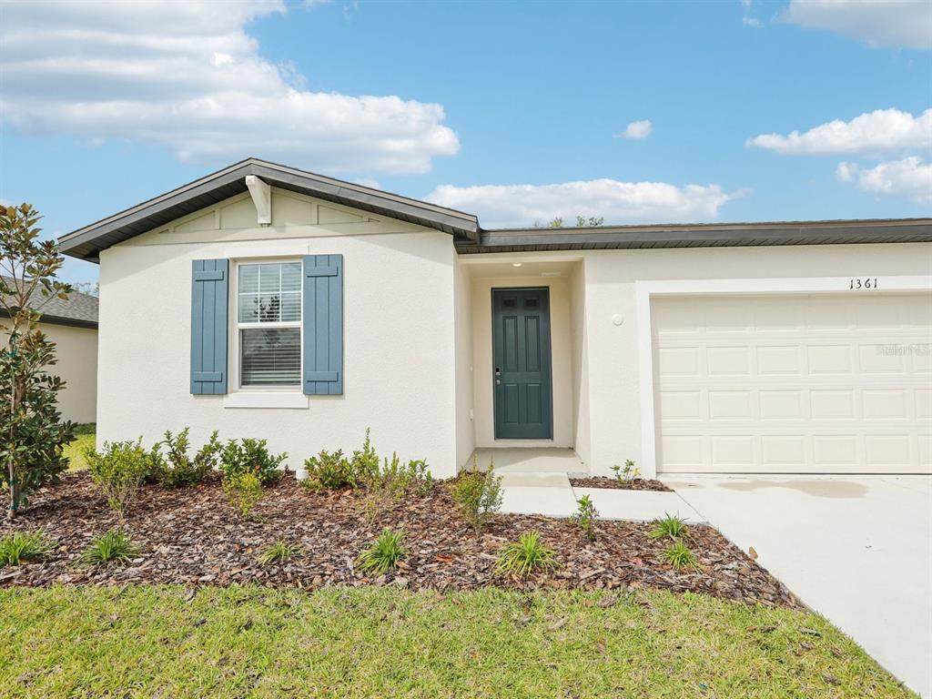 A single-story house with a white stucco exterior, blue shutters, and a garage — 1361 OAK VALLEY DRIVE, AUBURNDALE, FL