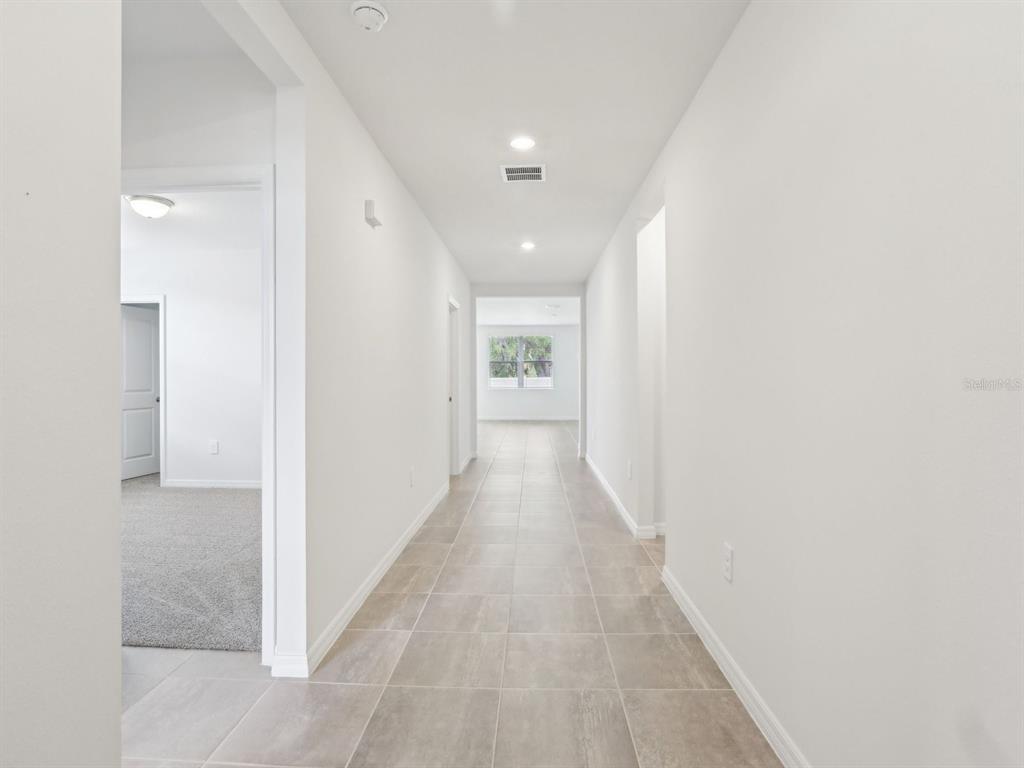 A long hallway with light-colored tile flooring leads toward a window at the far end — 1361 OAK VALLEY DRIVE, AUBURNDALE, FL