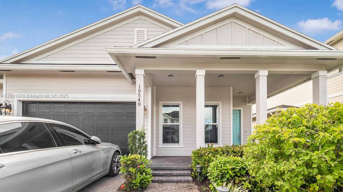 The exterior of a light-colored house features a covered porch, a garage, and landscaping — 19540 Wheelbarrow Bnd, Loxahatchee FL 33470, LOXAHATCHEE, FL
