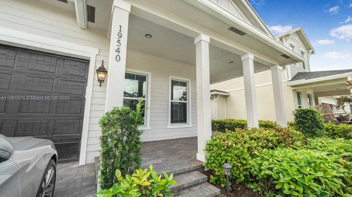 The exterior of a house features a covered porch, white siding, and a paved walkway — 19540 Wheelbarrow Bnd, Loxahatchee FL 33470, LOXAHATCHEE, FL