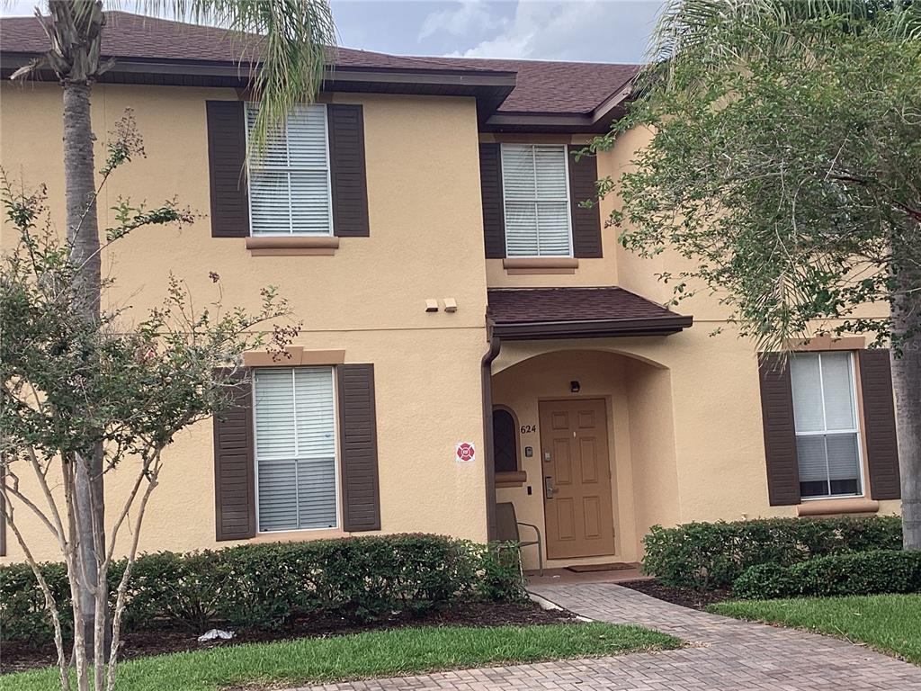 A two-story tan stucco townhouse with brown shutters and a paved walkway to the entrance — 624 TERRA LAGO STREET, DAVENPORT, FL