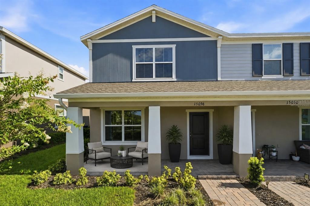 A two-story townhouse exterior features a covered front porch with seating and a blue gable — 15056 WINDFLOWER ALLEY, WINTER GARDEN, FL