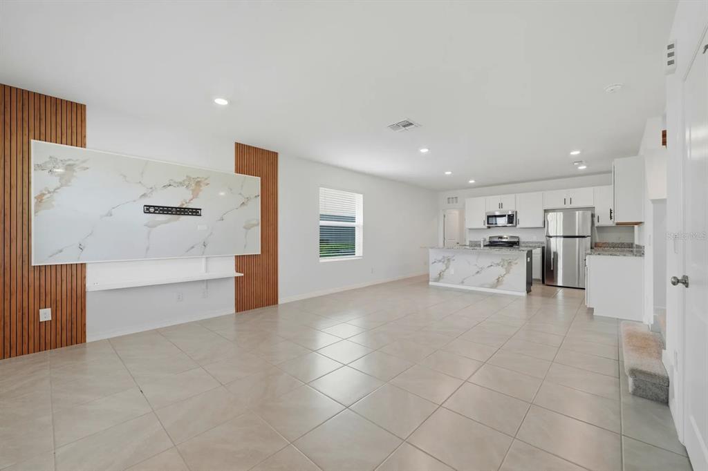 An open-concept living room and kitchen featuring tile floors, a marble accent wall, and cabinetry — 15056 WINDFLOWER ALLEY, WINTER GARDEN, FL
