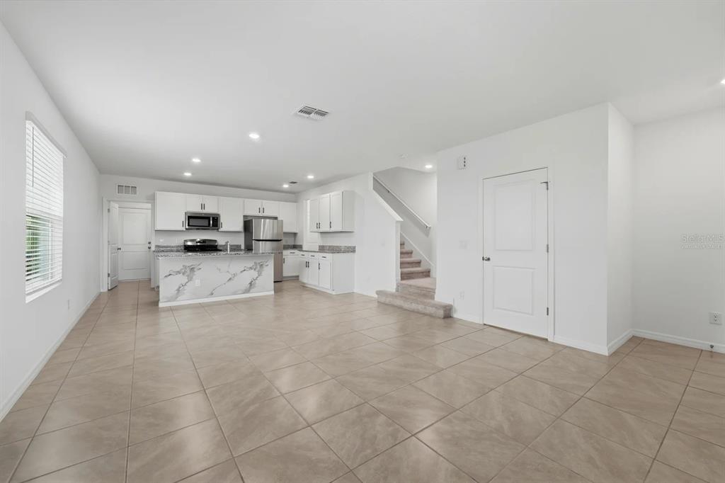 An open-concept kitchen with white cabinets and a marble-patterned island overlooks a tiled living area — 15056 WINDFLOWER ALLEY, WINTER GARDEN, FL