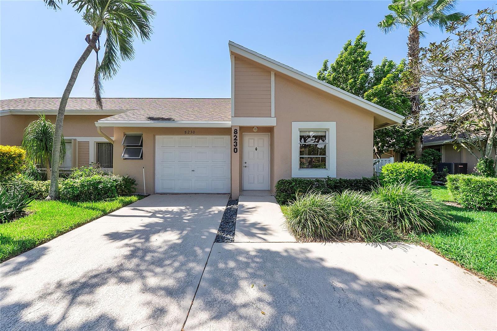 A tan single-story house features a white garage door, a front entrance, and a driveway — 8230 Springtree Road, Boca Raton FL 33496, BOCA RATON, FL