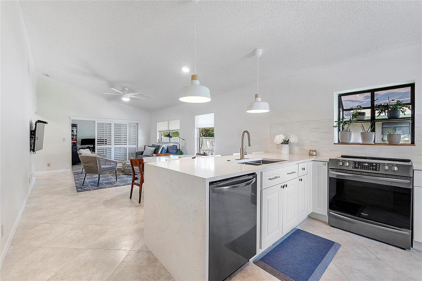 A kitchen with white cabinets and quartz countertops opens into a living area with tile — 8230 Springtree Road, Boca Raton FL 33496, BOCA RATON, FL