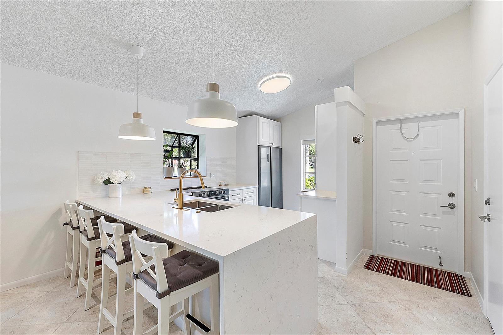 A bright kitchen features a white quartz island with bar seating and modern pendant lights — 8230 Springtree Road, Boca Raton FL 33496, BOCA RATON, FL