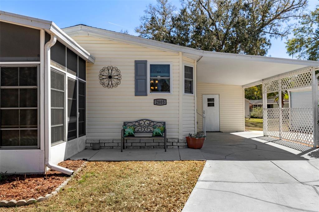 A light-colored mobile home features a screened-in porch, a concrete carport, and a front bench — 2805 KINGSWOOD CIRCLE, BROOKSVILLE, FL