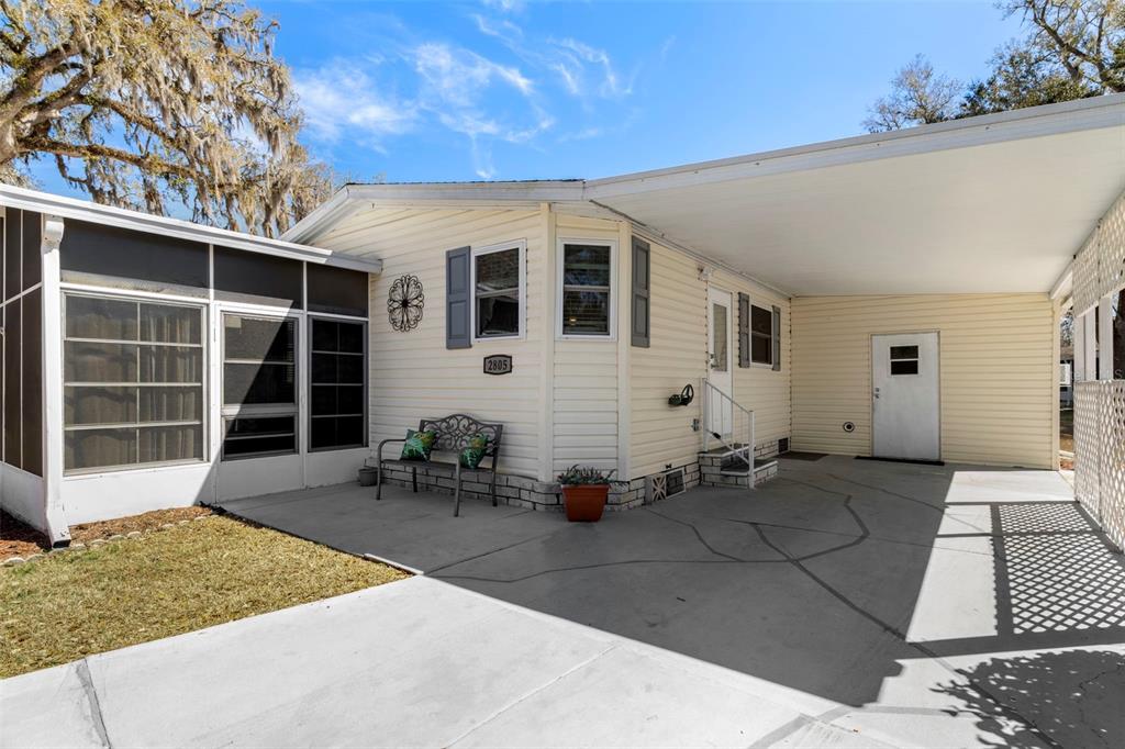 A light-colored mobile home exterior features a concrete driveway, a carport, and a screened porch — 2805 KINGSWOOD CIRCLE, BROOKSVILLE, FL