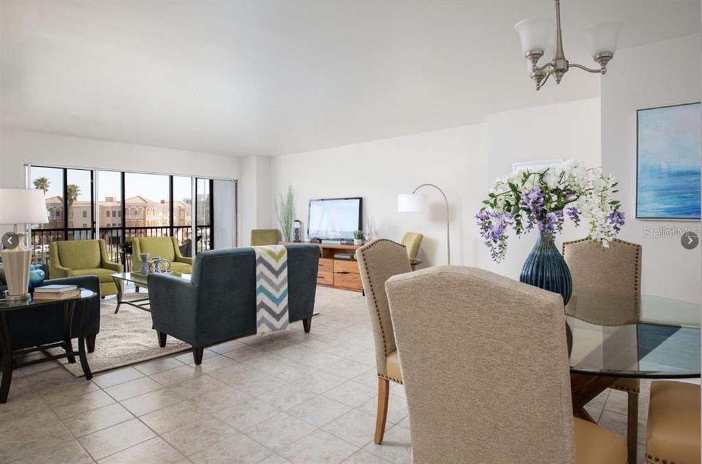 A bright open-concept living and dining area with tile floors and a balcony view — 10355 PARADISE BOULEVARD UNIT 211, TREASURE ISLAND, FL