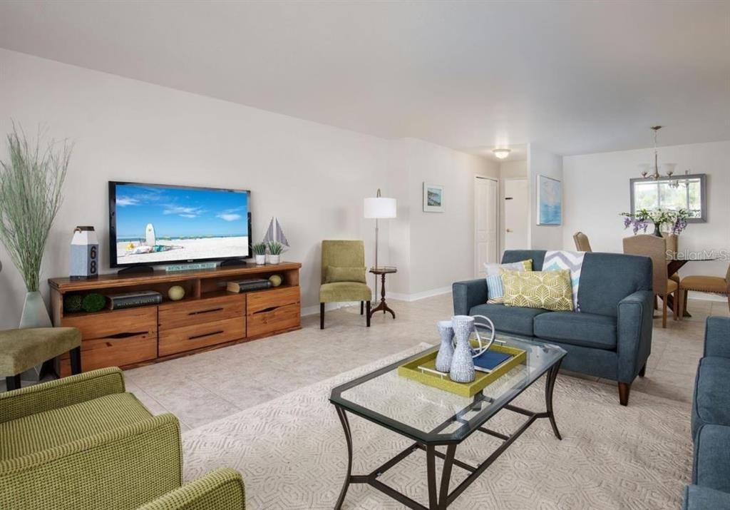 A living room with a television on a wooden console, blue sofa, and green chairs — 10355 PARADISE BOULEVARD UNIT 211, TREASURE ISLAND, FL