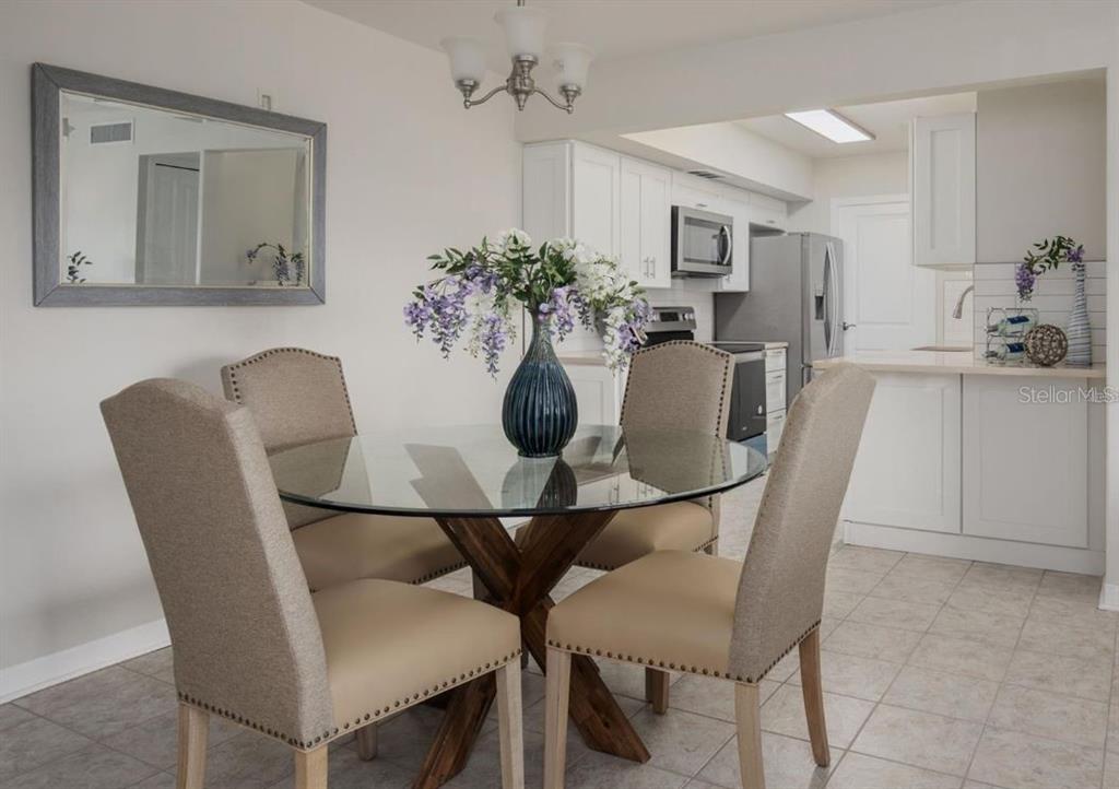 A dining area with a glass-topped table and four chairs sits before an open kitchen — 10355 PARADISE BOULEVARD UNIT 211, TREASURE ISLAND, FL