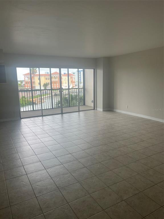 An empty room with light-colored tile flooring and a sliding glass door leading to a balcony — 10355 PARADISE BOULEVARD UNIT 211, TREASURE ISLAND, FL