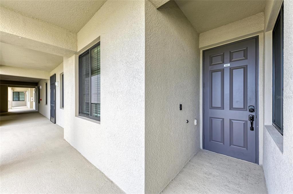 An exterior view of a building corridor featuring a gray front door labeled 306 — 18114 GAWTHROP DRIVE UNIT 306, BRADENTON, FL
