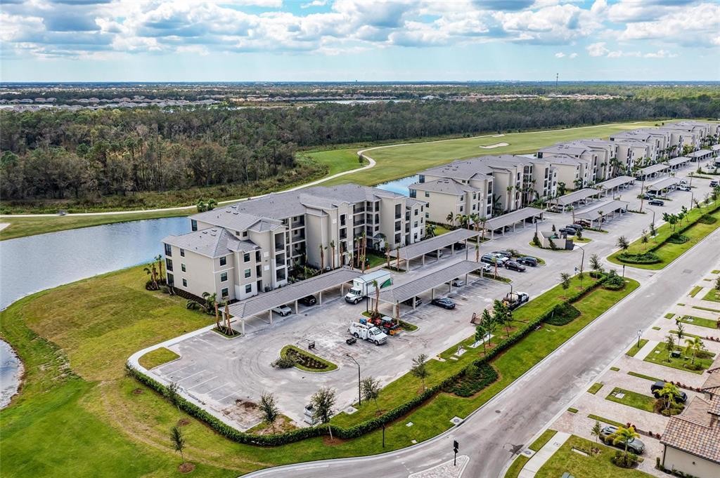An aerial view shows a multi-story apartment building with covered parking and a nearby pond — 18114 GAWTHROP DRIVE UNIT 306, BRADENTON, FL