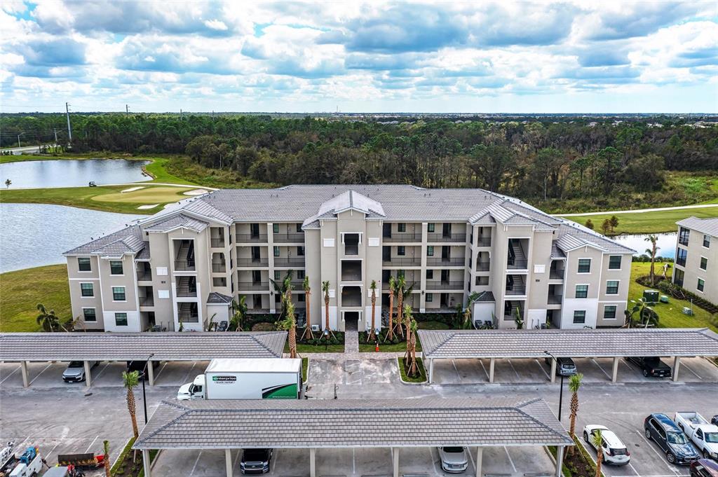 An aerial view shows a multi-story apartment building with covered parking and a nearby pond — 18114 GAWTHROP DRIVE UNIT 306, BRADENTON, FL
