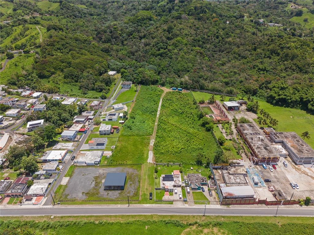 An aerial view shows a large, undeveloped grassy lot situated between residential and commercial buildings — PR 182 KM 3.3 BO. CALABAZAS, YABUCOA, PR