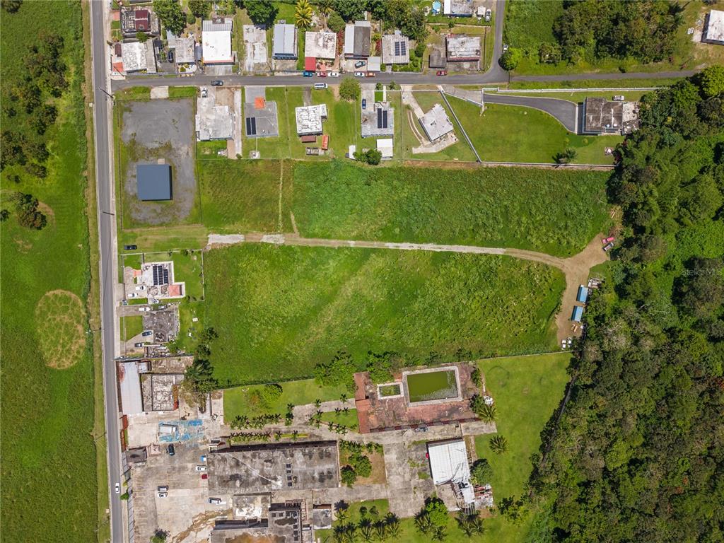 An aerial view shows a large grassy lot surrounded by residential buildings and dense vegetation — PR 182 KM 3.3 BO. CALABAZAS, YABUCOA, PR
