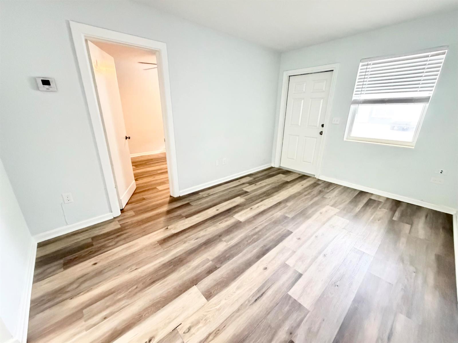 An empty room features light-colored walls, wood-look plank flooring, a doorway, and a window — 1502 N J Street # 2, FL 33460, FL