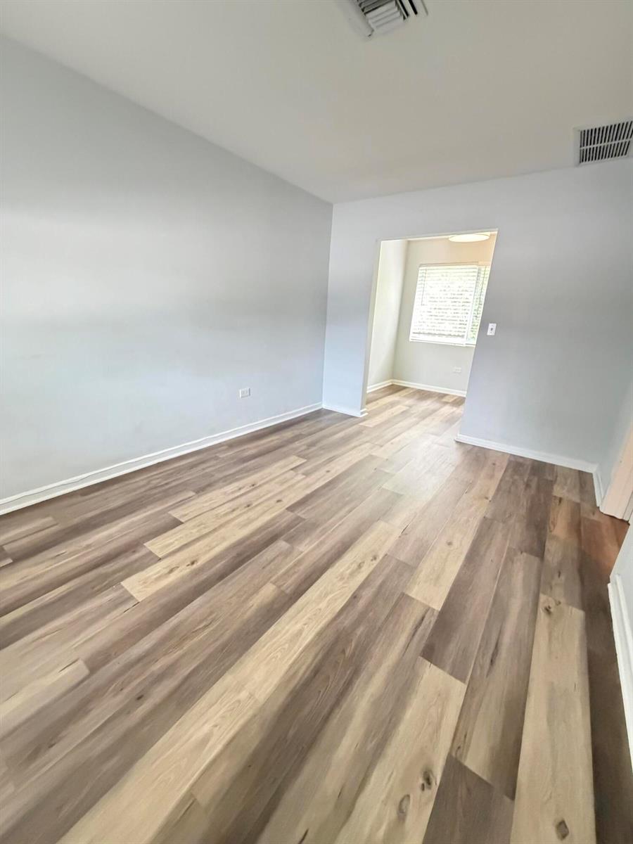 An empty room with light gray walls and wood-look plank flooring leads to an adjacent space — 1502 N J Street # 2, FL 33460, FL
