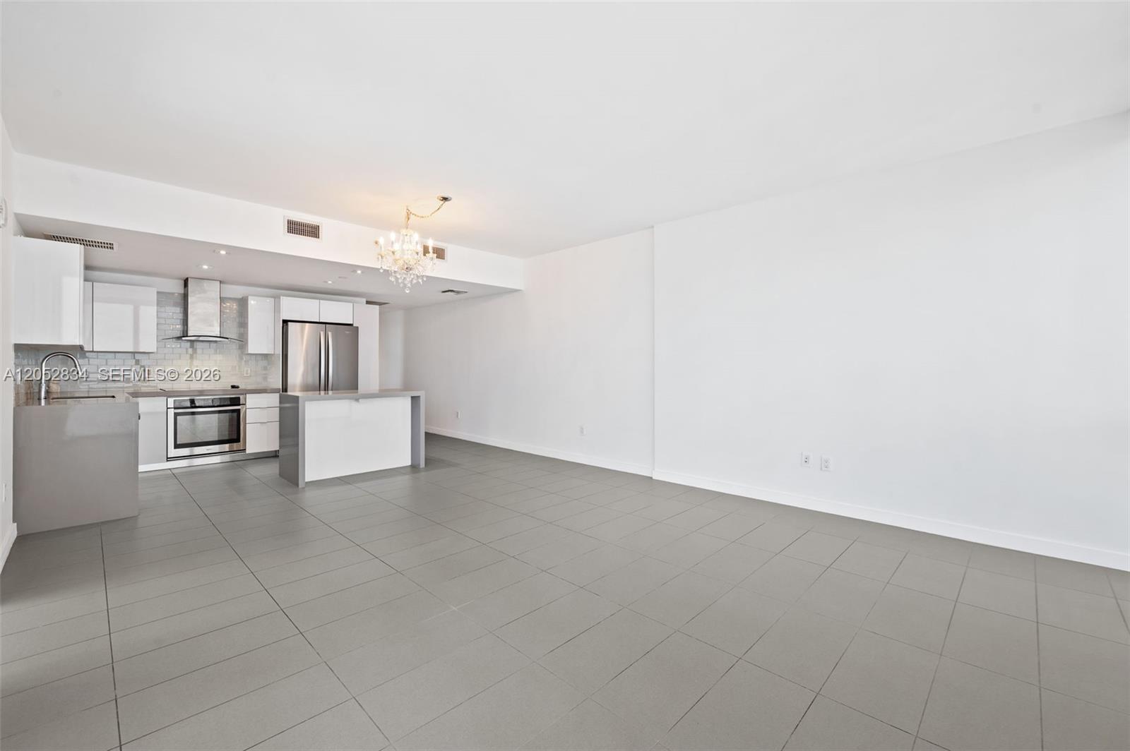 An open-concept kitchen and living area features white cabinetry, stainless steel appliances, and gray tile flooring — 1600 NE 1st Ave # 2420, Miami FL 33132, MIAMI, FL