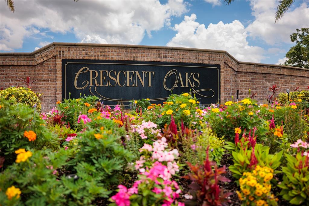 A brick wall with a Crescent Oaks sign sits behind a colorful flower garden — 1338 DARTFORD DRIVE, TARPON SPRINGS, FL
