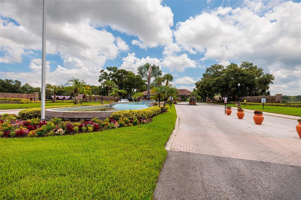 A paved driveway leads to a gated community entrance featuring a fountain and landscaping — 1338 DARTFORD DRIVE, TARPON SPRINGS, FL