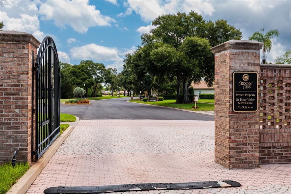 A brick entrance gate leads into the Crescent Oaks residential community under a blue sky — 1338 DARTFORD DRIVE, TARPON SPRINGS, FL