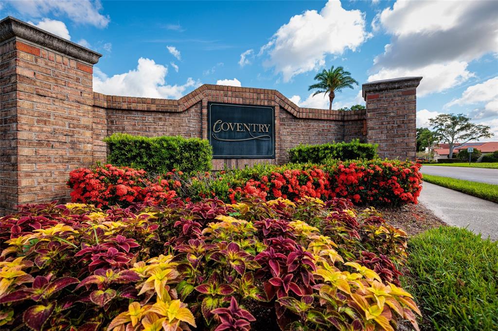 A brick entrance sign for a community named Coventry surrounded by colorful landscaping and flowers — 1338 DARTFORD DRIVE, TARPON SPRINGS, FL