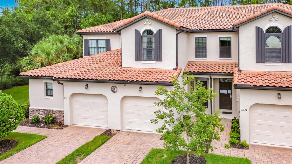 An exterior view of a two-story stucco townhouse with a tile roof and three garage doors — 8223 ROSEVILLE ROAD, DAVENPORT, FL