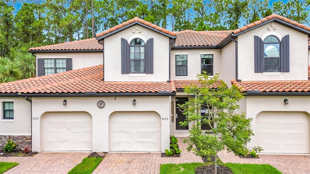 A two-story townhouse with a tile roof, three garage doors, and beige stucco exterior — 8223 ROSEVILLE ROAD, DAVENPORT, FL