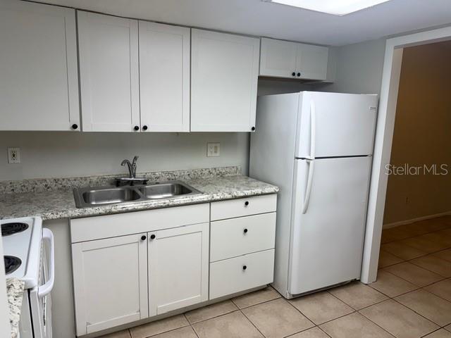 A kitchen features white cabinets, a double-basin sink, a white refrigerator, and tiled flooring — 7309 ABONADO ROAD UNIT 7309, TAMPA, FL