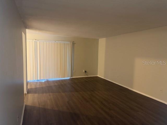 An empty living room features light gray walls, dark wood-look flooring, and vertical window blinds — 7309 ABONADO ROAD UNIT 7309, TAMPA, FL