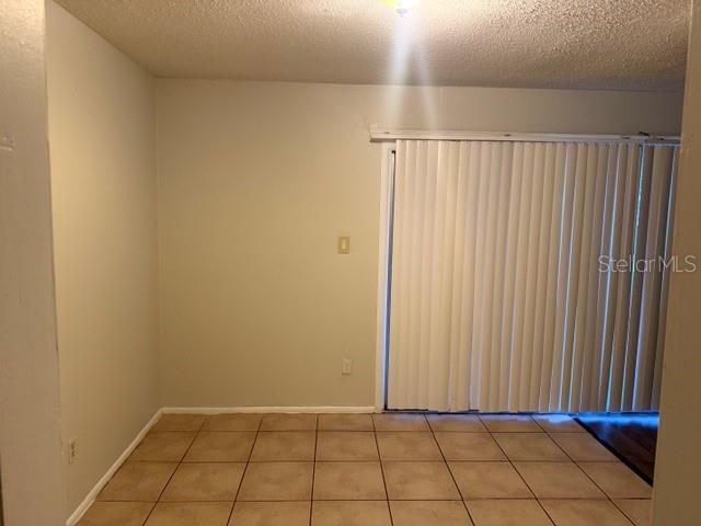 A room with beige tile flooring and vertical blinds covering a sliding glass door — 7309 ABONADO ROAD UNIT 7309, TAMPA, FL