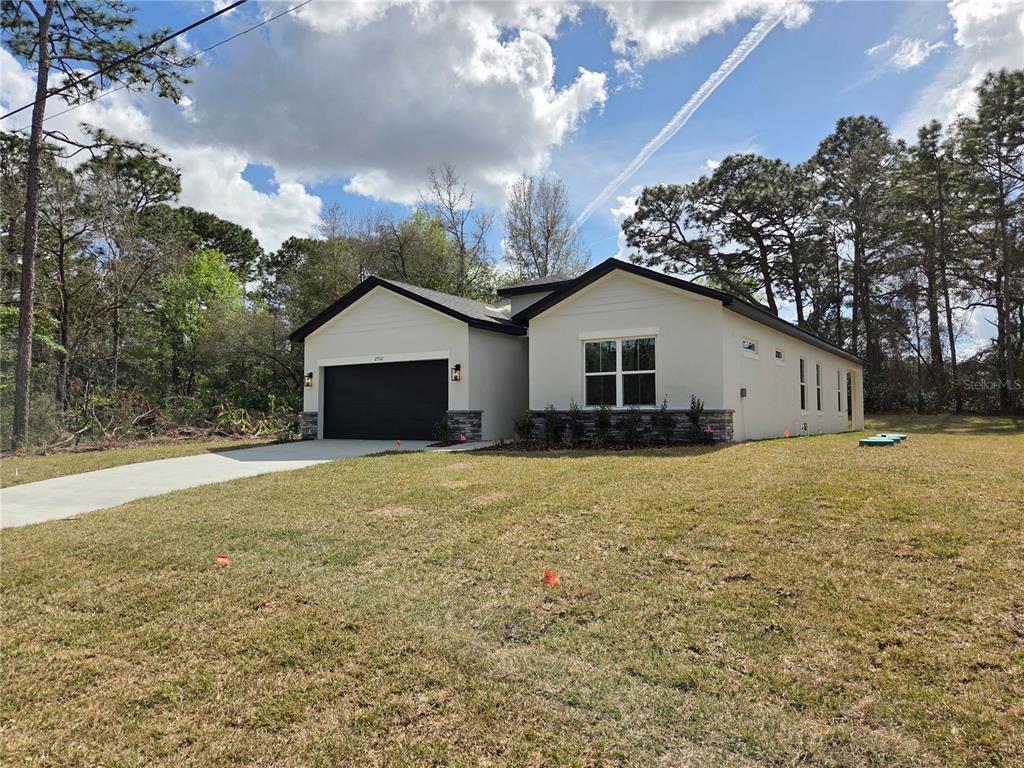 A single-story house with a black garage door, stone accents, and a concrete driveway — 2992 W HAMLET PLACE, DUNNELLON, FL