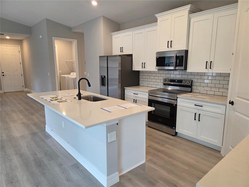 A modern kitchen features white cabinets, stainless steel appliances, a quartz island, and light flooring — 2992 W HAMLET PLACE, DUNNELLON, FL